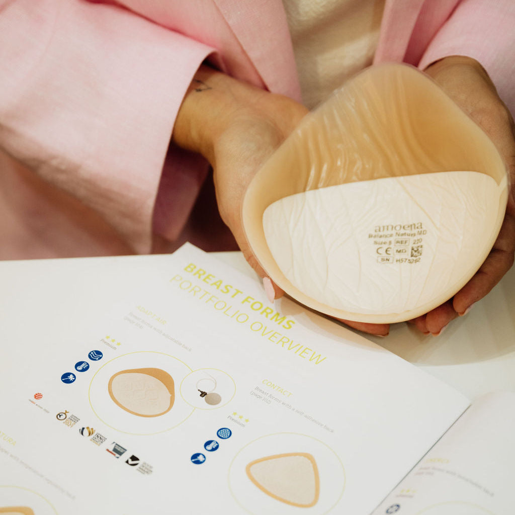 Hand holding a silicone breast form with a pink garment in the background
