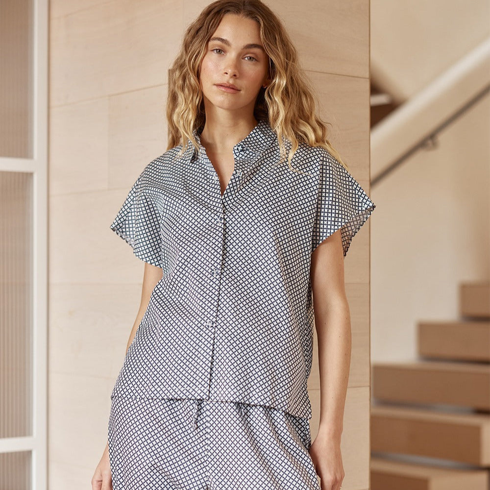 Woman wearing a checkered outfit standing in a home setting with wooden stairs.