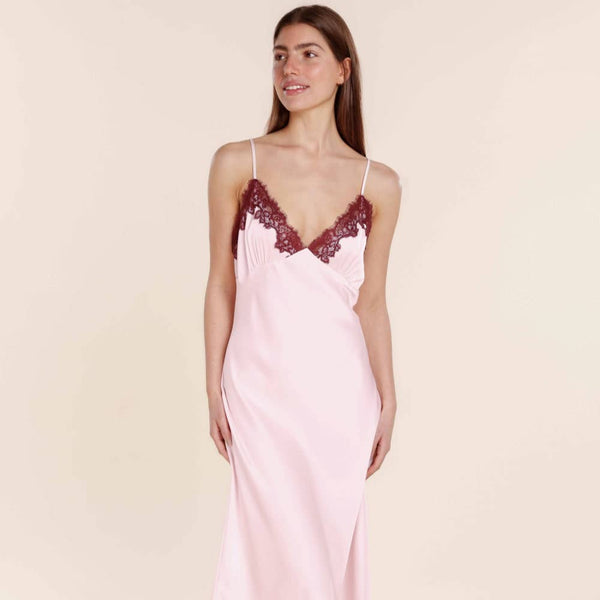 Woman wearing a pink slip dress with lace trim on a beige background