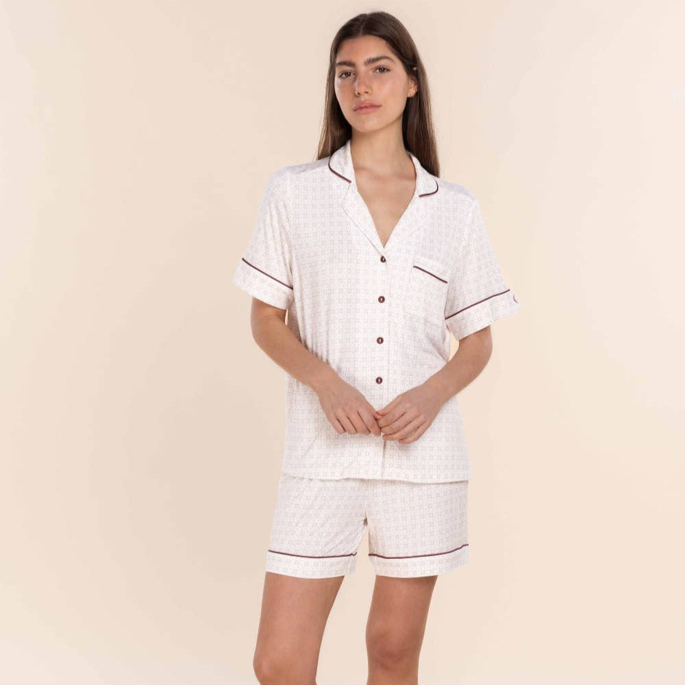 Woman wearing a white pajama set with black piping on a beige background