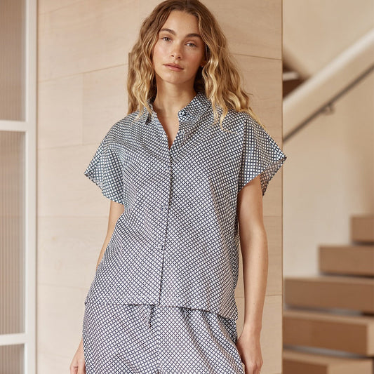 Woman wearing a checkered outfit standing in a home setting with wooden stairs.
