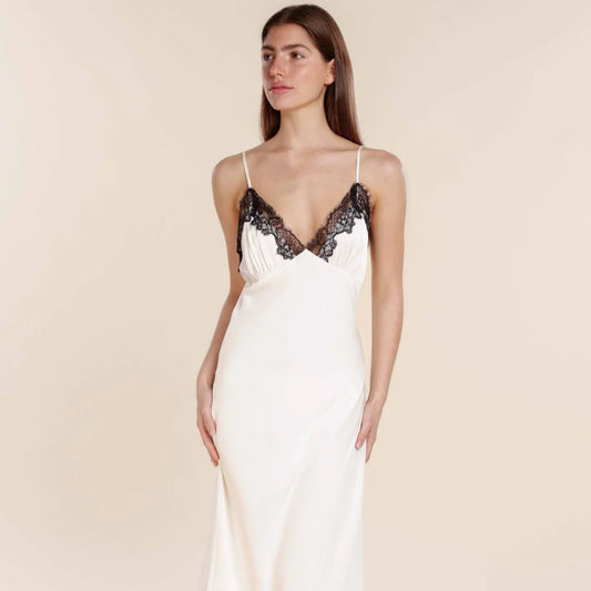Woman wearing a white slip dress with black lace details on a beige background